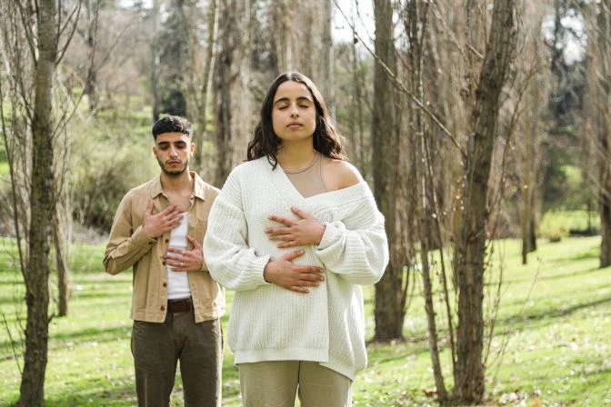 Couple in a forest breathing deeply with hands on their bodies